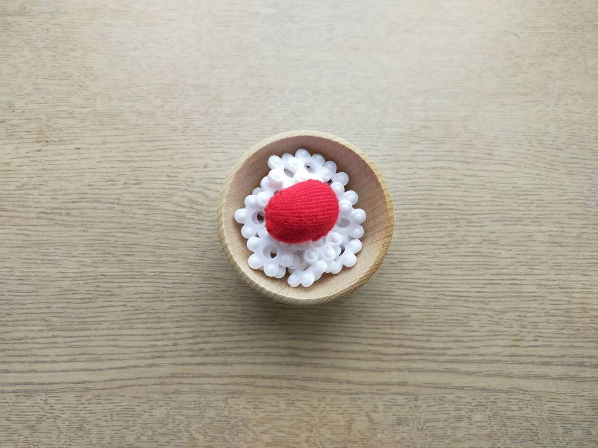 木の器に白い飾りと赤い毛糸玉を入れてごはんに見立てた具材