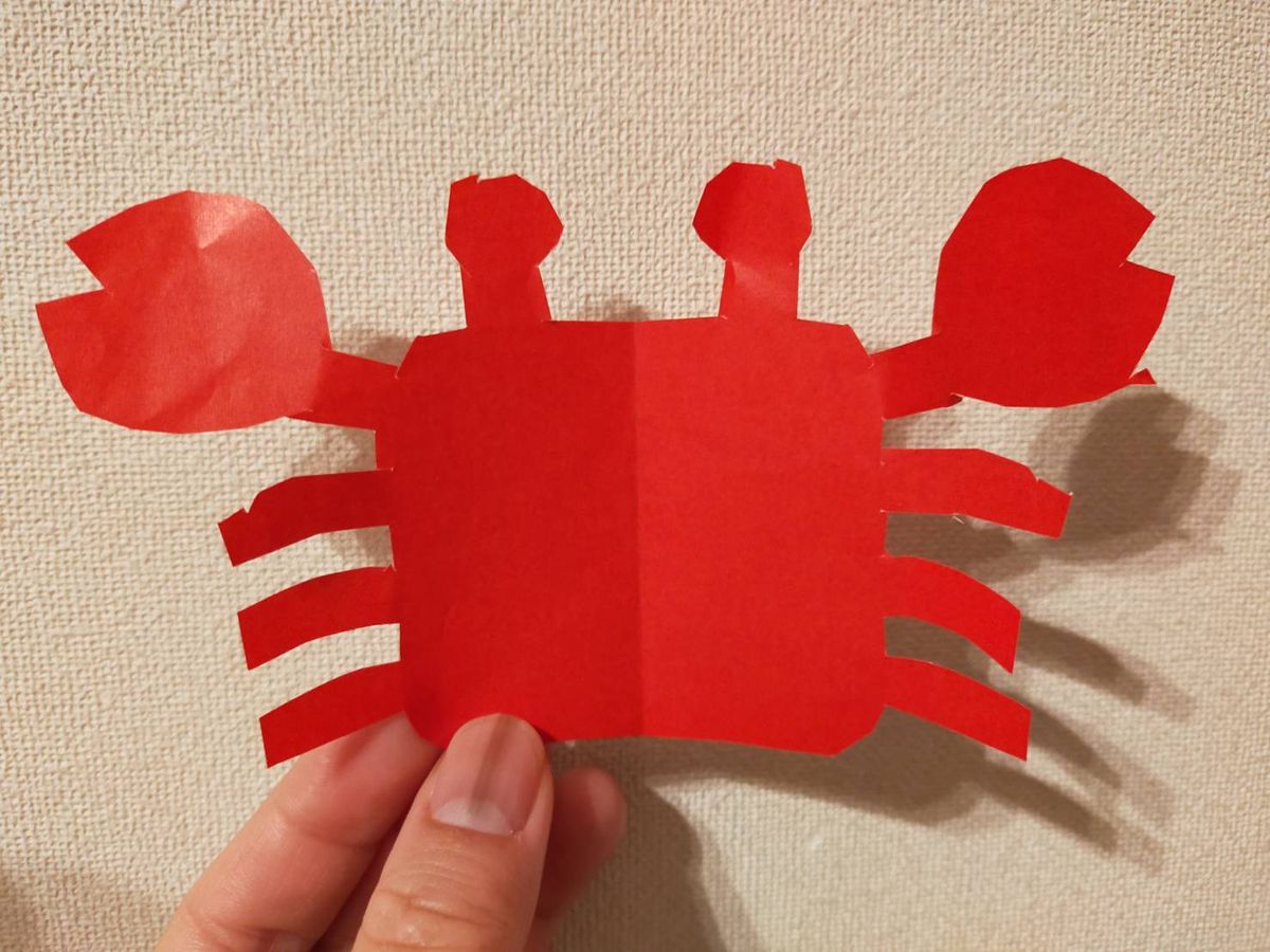 折り紙を切って作ったカニを手に持って見せている